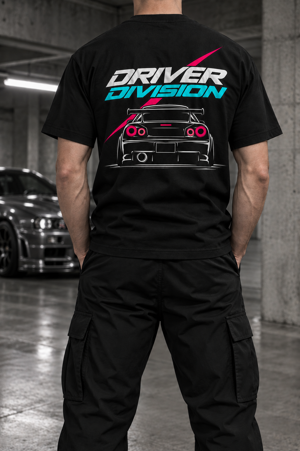 Rear view of a black Staple Tee with a white and turquoise DRIVER DIVISION logo, pink accents and a car back print